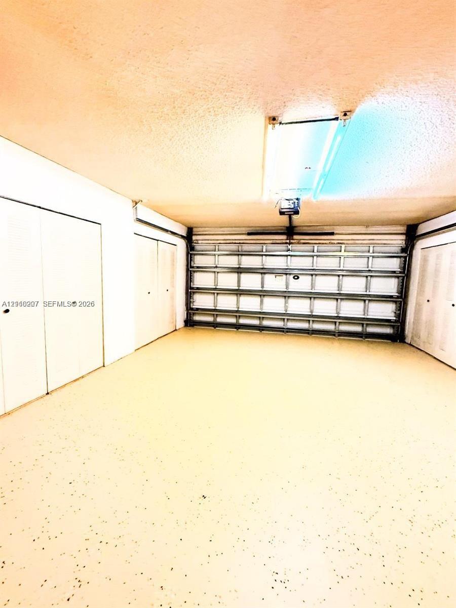 Garage featuring an epoxy-coated floor, automatic sectional door, and three sets of double-door built-in storage closets