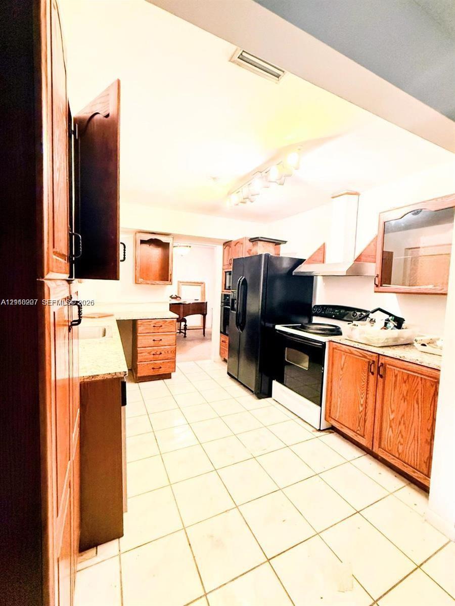 Kitchen featuring wood cabinetry, stone countertops, ceramic tile flooring, a stainless steel range hood, and track lighting