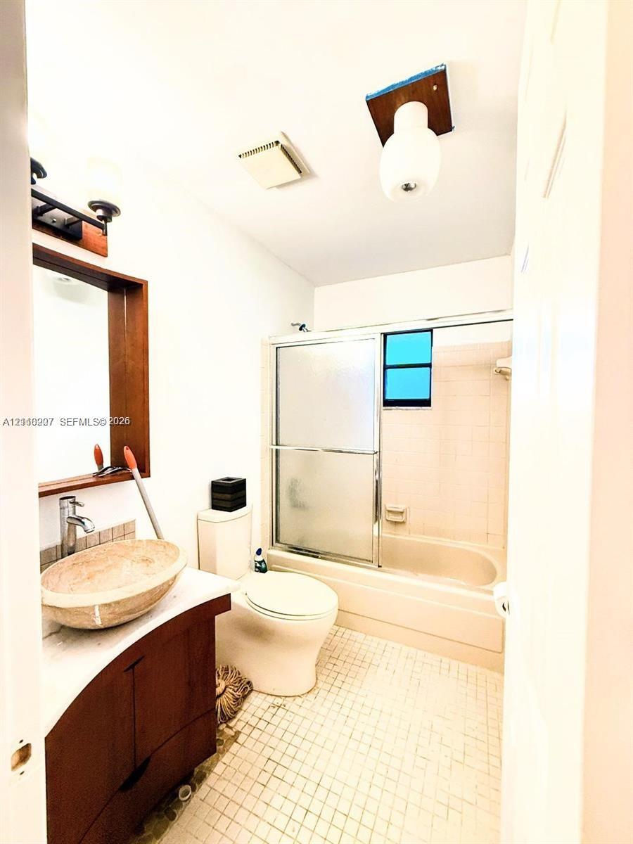 Bathroom featuring a wood-finish vanity, stone vessel sink, framed mirror, and a combination bathtub and shower enclosure with sliding glass doors