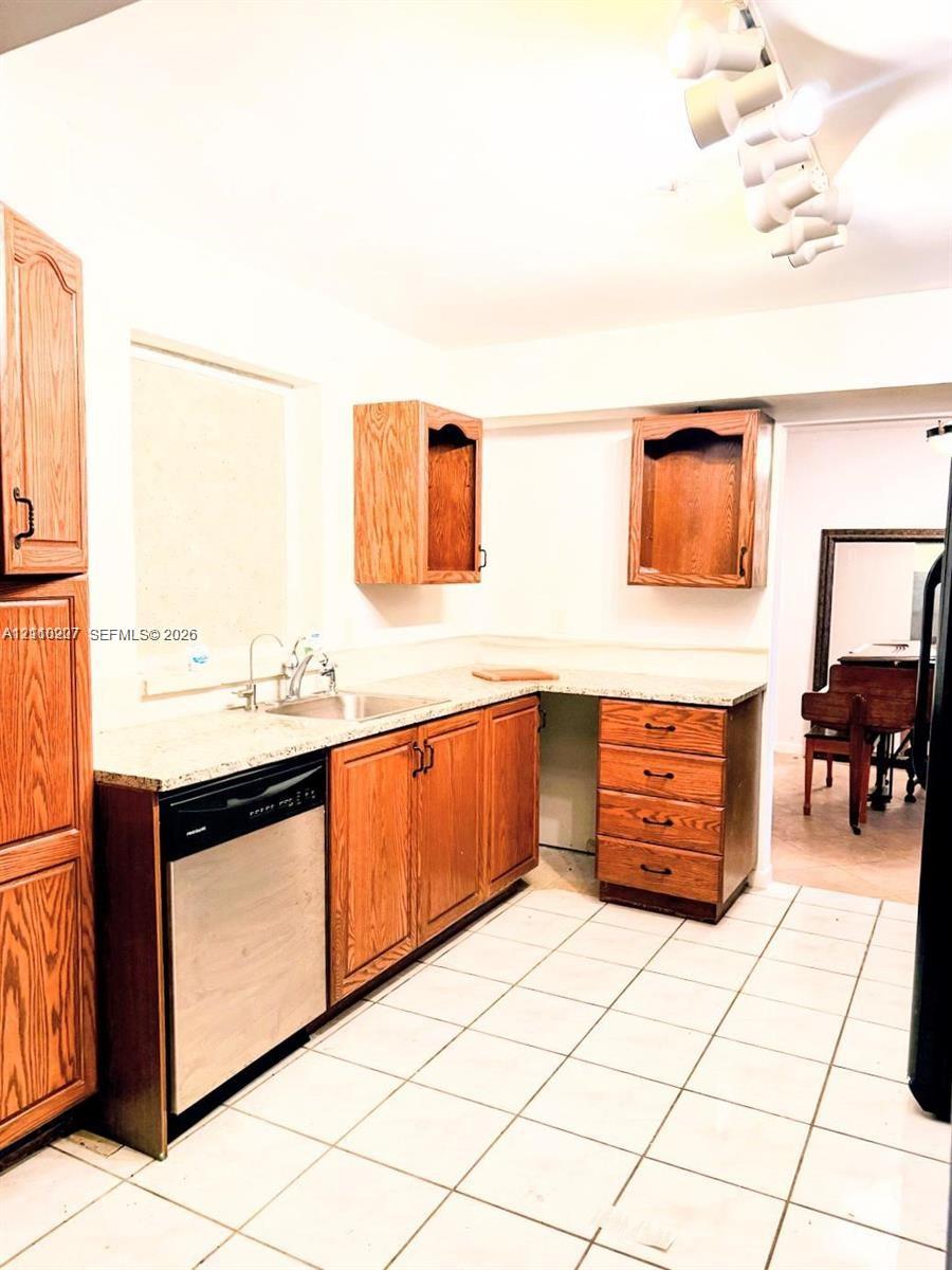 Kitchen featuring wood cabinetry, stone-finish countertops, stainless steel dishwasher, undermount sink, and ceramic tile flooring