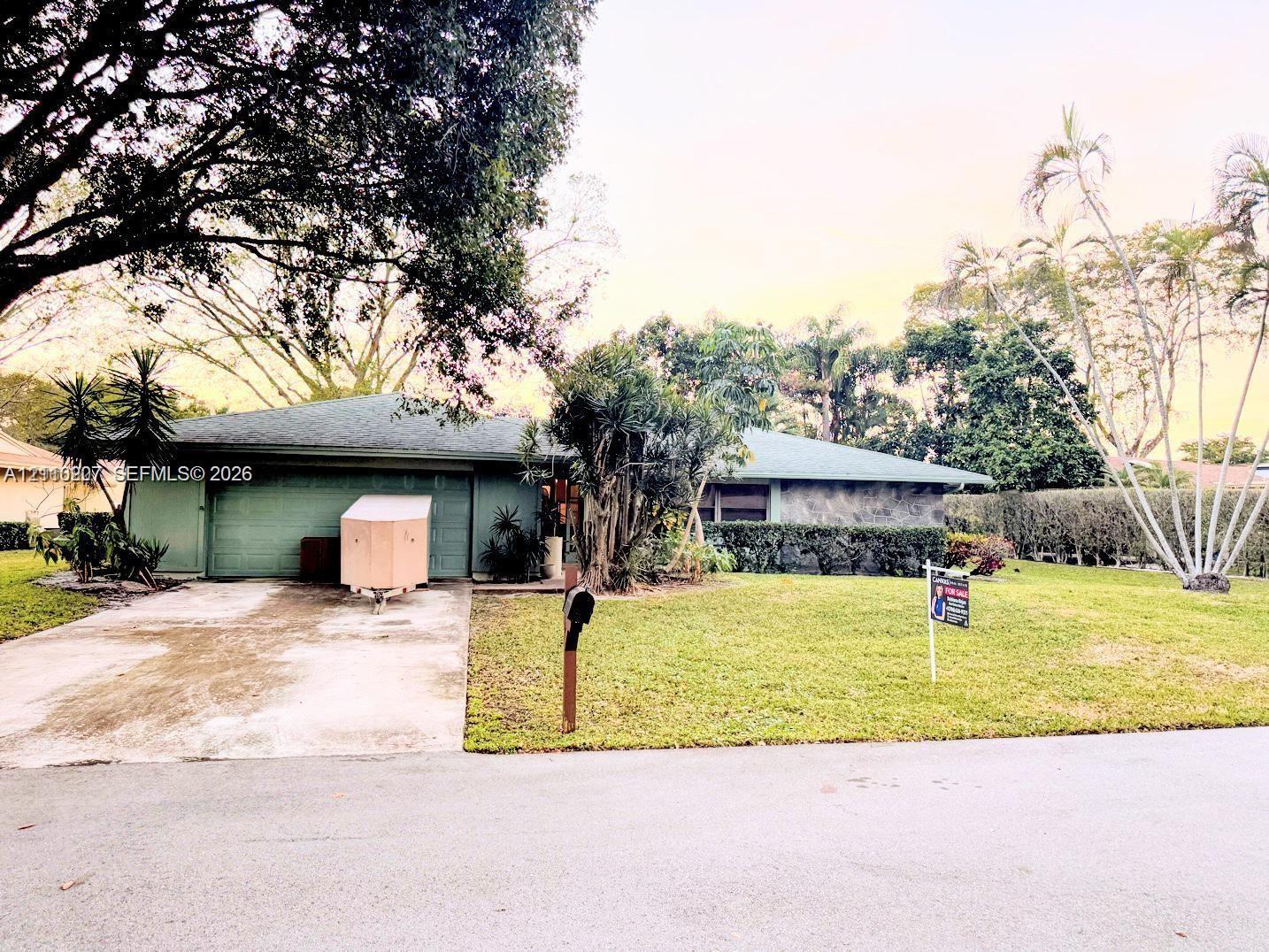 Single-story residence featuring a concrete driveway, two-car garage, stone facade detailing, and established landscaping Single-story residence featuring a concrete driveway, two-car garage, stone facade detailing, and established landscaping