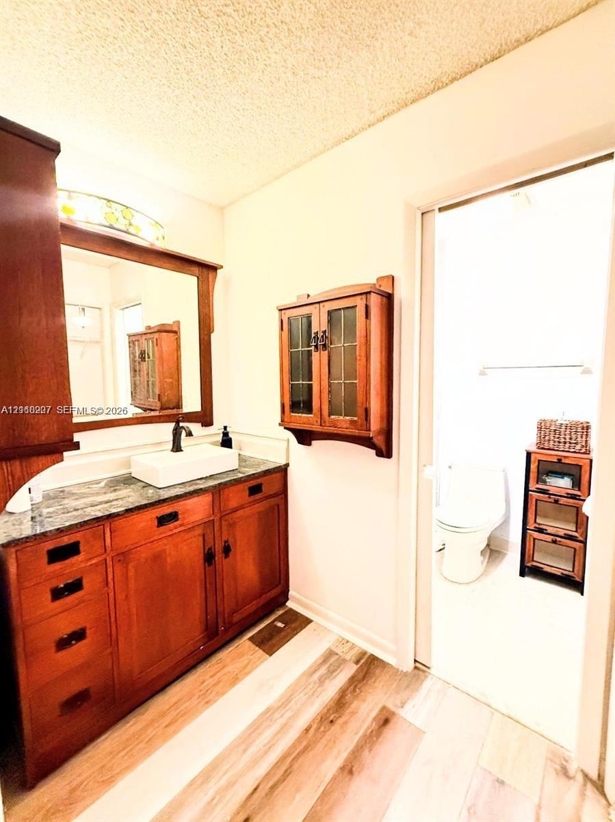 Bathroom featuring stained wood cabinetry, rectangular vessel sink, stone-finish countertop, wall-mounted wood-framed storage, and wood-finish flooring