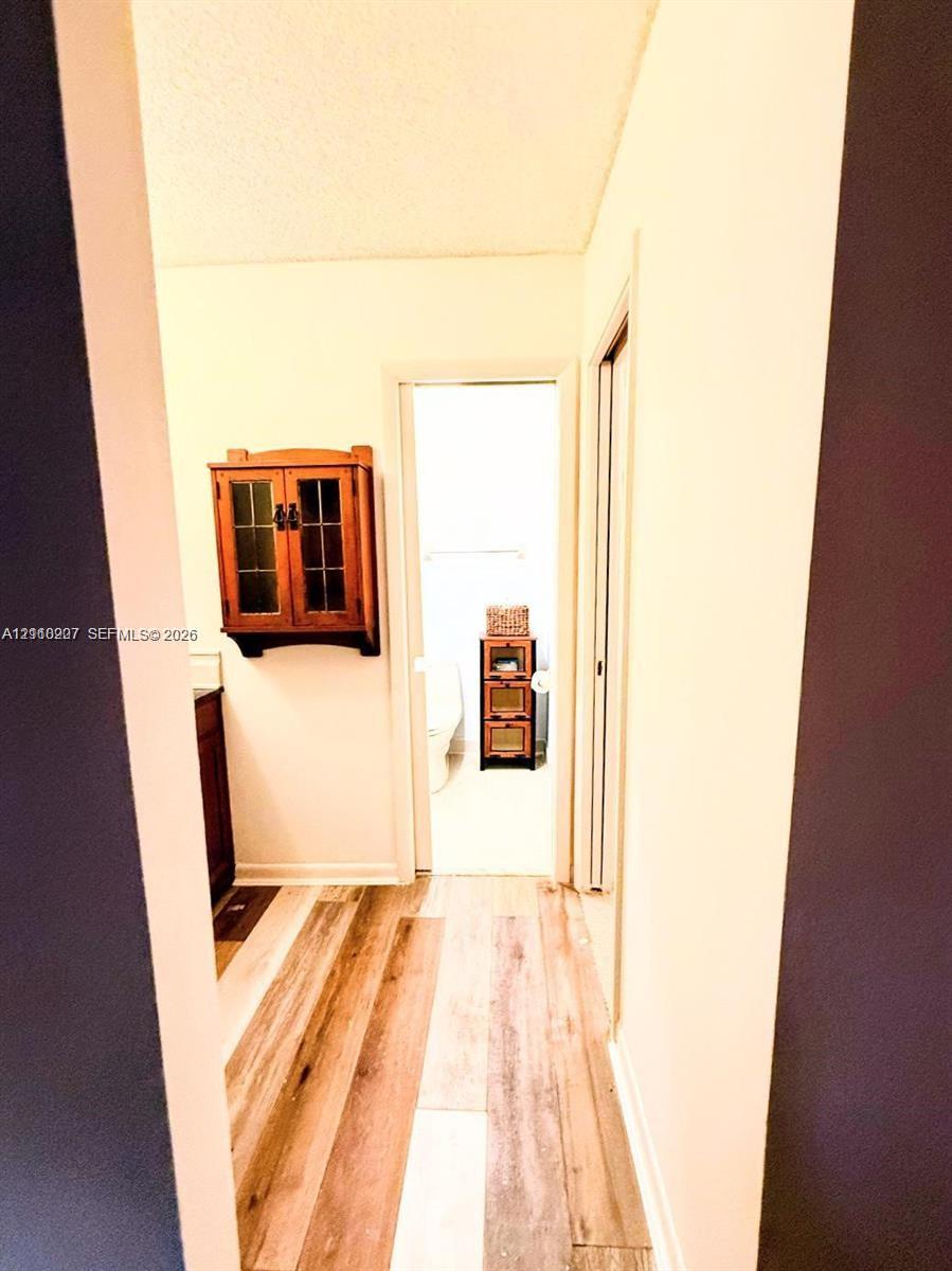 Hallway featuring wood-finish flooring and a wall-mounted wood-finish cabinet with glass paneling