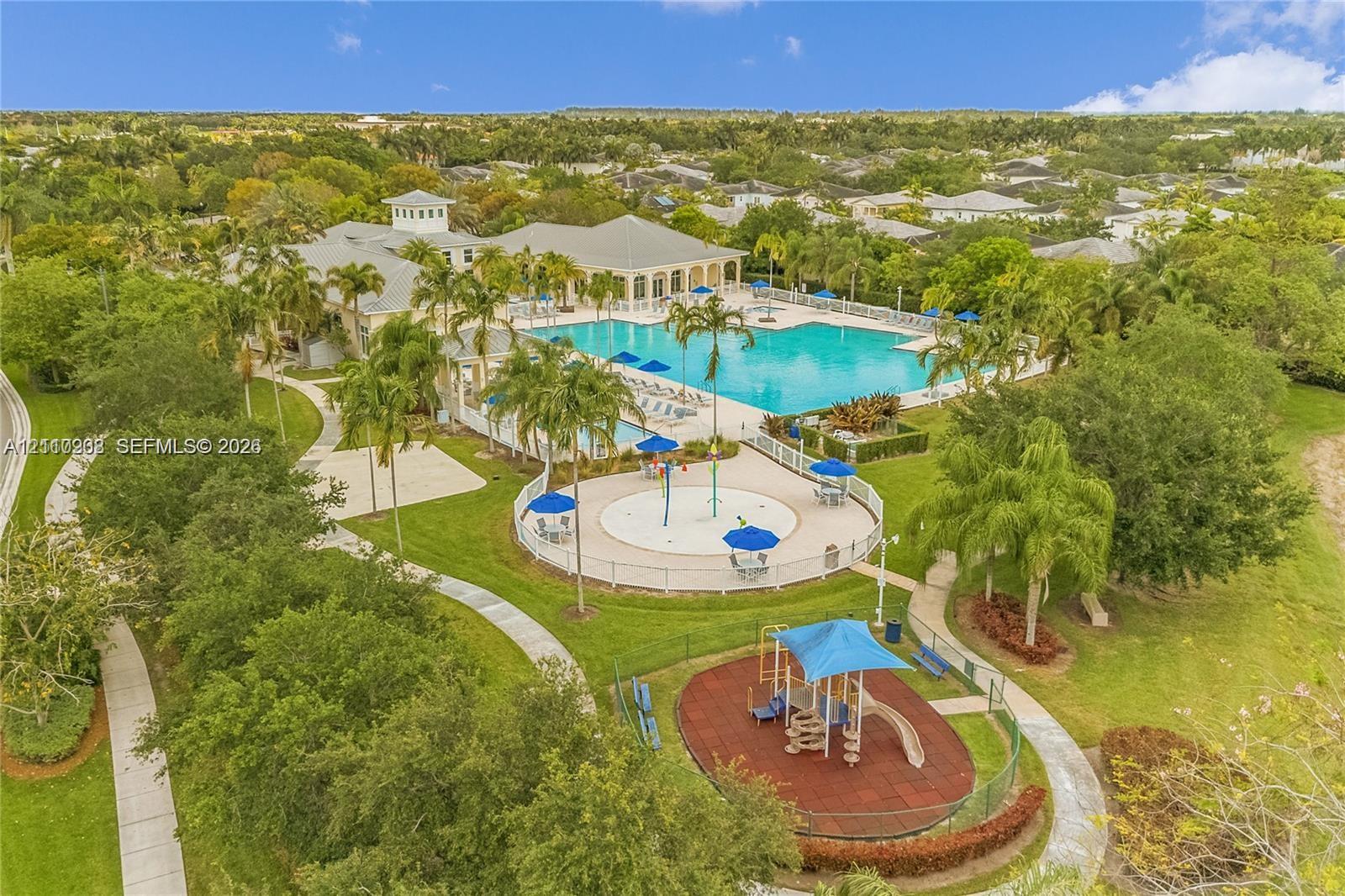 Recreational complex featuring a large swimming pool, splash pad, paved pathways, and an outdoor play area situated within a landscaped setting
