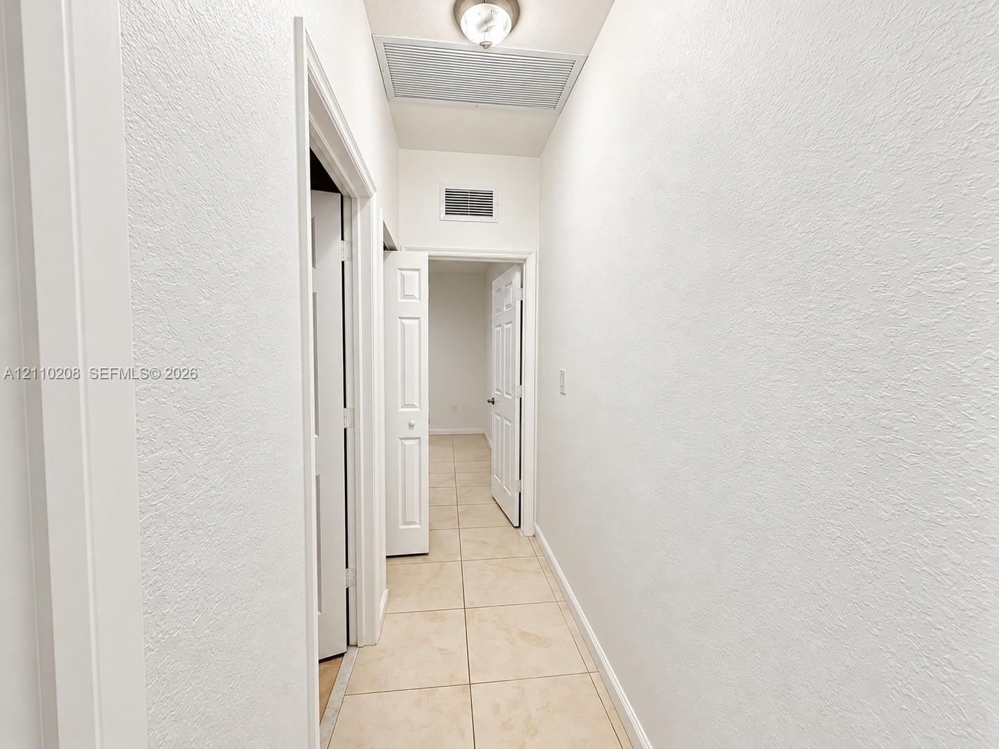 Interior hallway featuring neutral ceramic tile flooring, textured wall finishes, and multi-panel interior doors