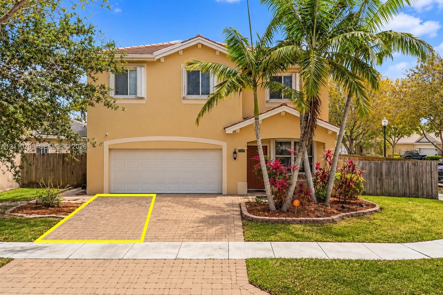 Two-story stucco exterior featuring a paved stone driveway, an integrated two-car garage, and landscaped garden beds with mature palms Two-story stucco exterior featuring a paved stone driveway, an integrated two-car garage, and landscaped garden beds with mature palms