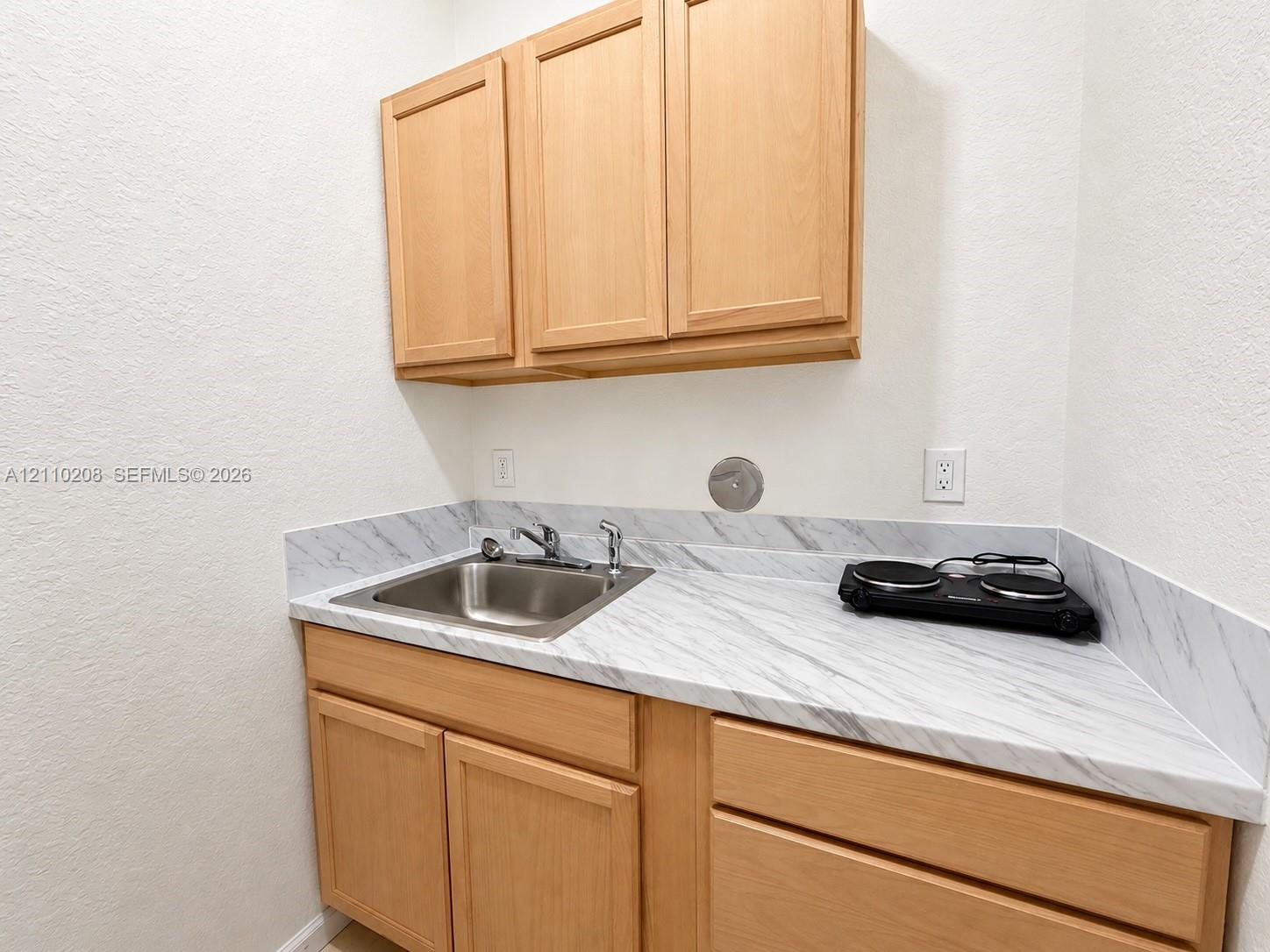 Light wood cabinetry featuring upper and lower storage, stone-patterned countertop, and integrated stainless steel sink with metal faucet