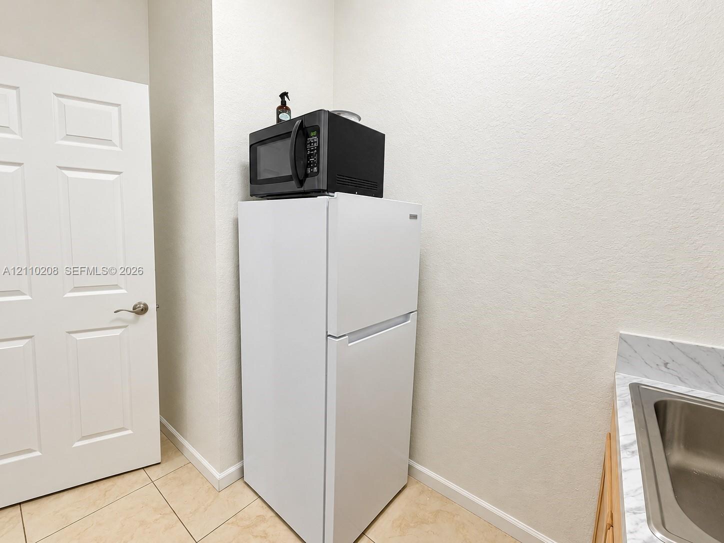 Utility area featuring light-toned tile flooring, a solid-core six-panel door, and a built-in countertop with an integrated stainless steel sink basin
