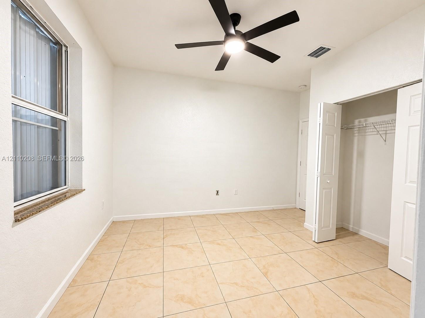 Neutral-toned tile flooring, multi-pane window with stone-finish sill, integrated ceiling fan with light fixture, and closet with bifold doors