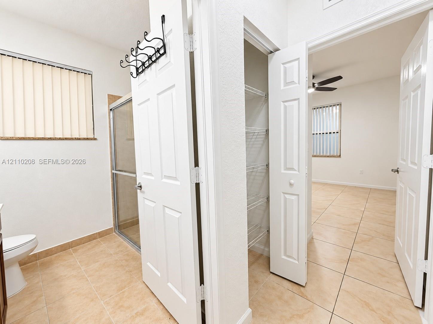 Neutral-toned tile flooring, built-in wire shelving, glass-enclosed shower, and multi-panel interior doors