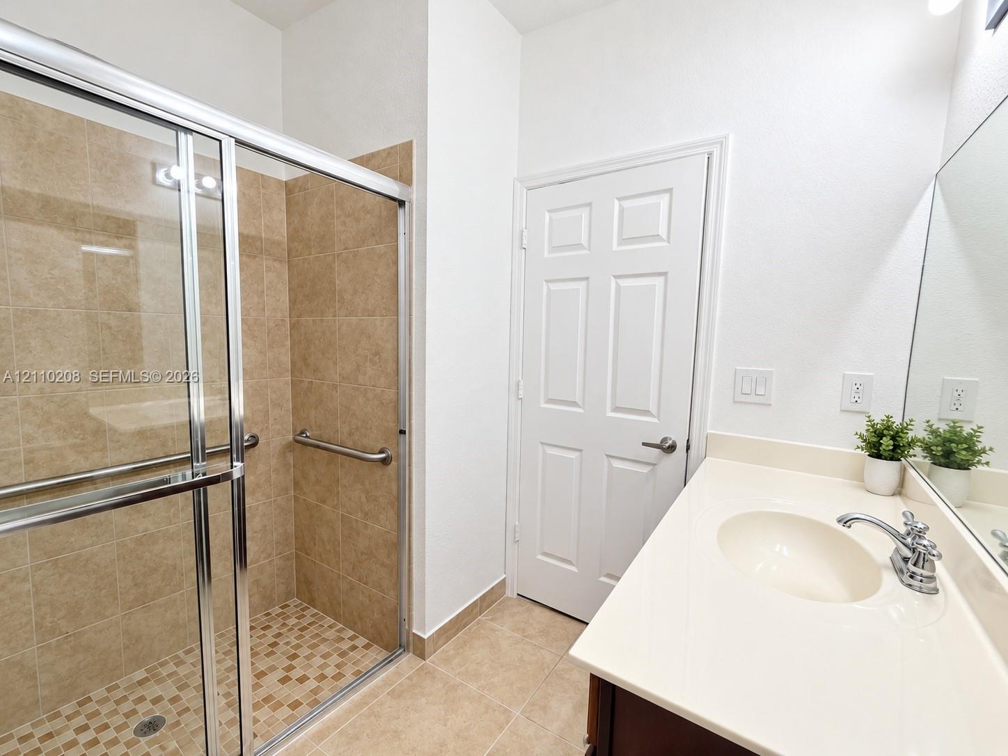 Walk-in shower with tiled surround and metal grab bars, paired with a solid-surface countertop and integrated sink