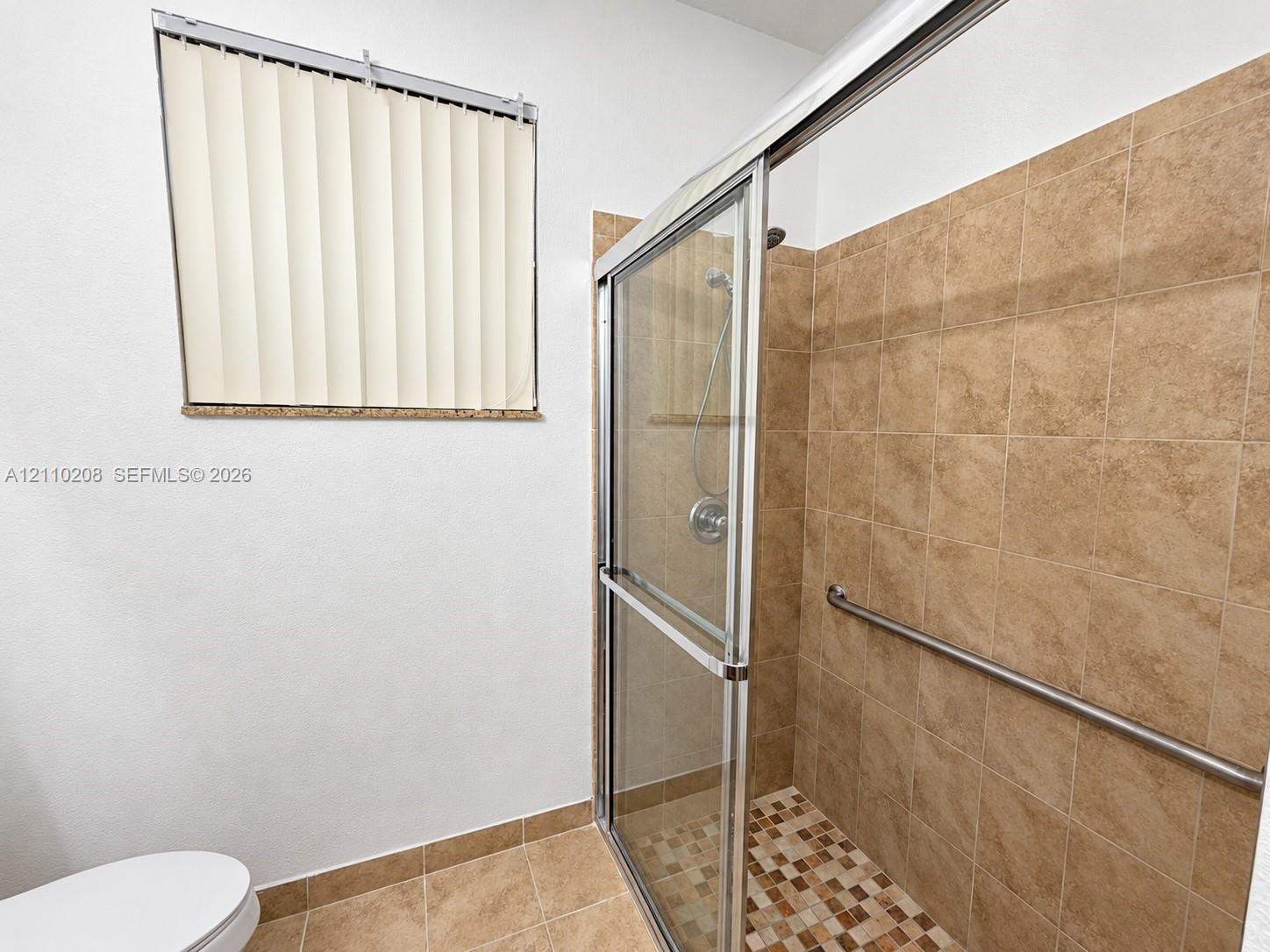 Walk-in shower with sliding glass doors, neutral tile surround, integrated metal grab bar, and a mosaic tile shower floor
