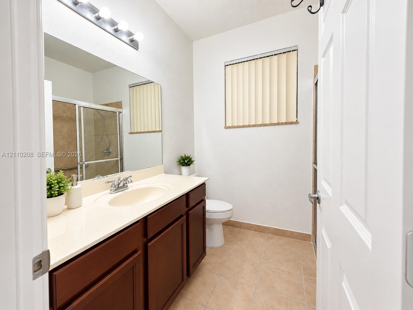 Bathroom featuring a solid-surface vanity countertop, wood cabinetry, large vanity mirror, four-bulb light fixture, and tile flooring
