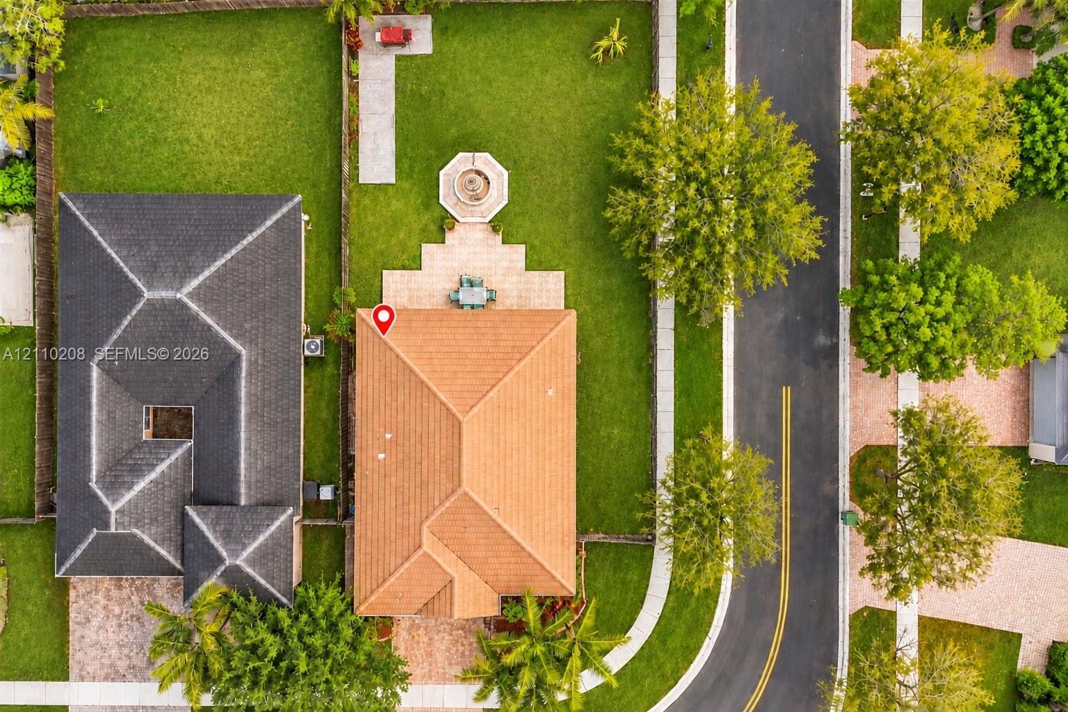 Aerial perspective of a property featuring a tile roof, paved rear patio, stone-finish fountain, fenced perimeter, and manicured lawn