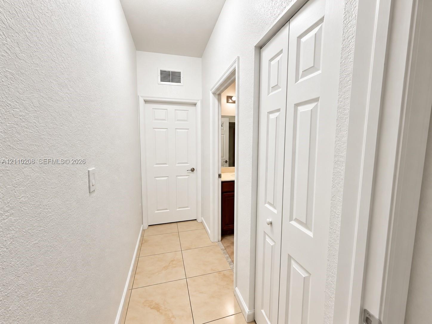 Neutral-toned floor tiling, textured walls, white six-panel interior door, and white bi-fold closet doors