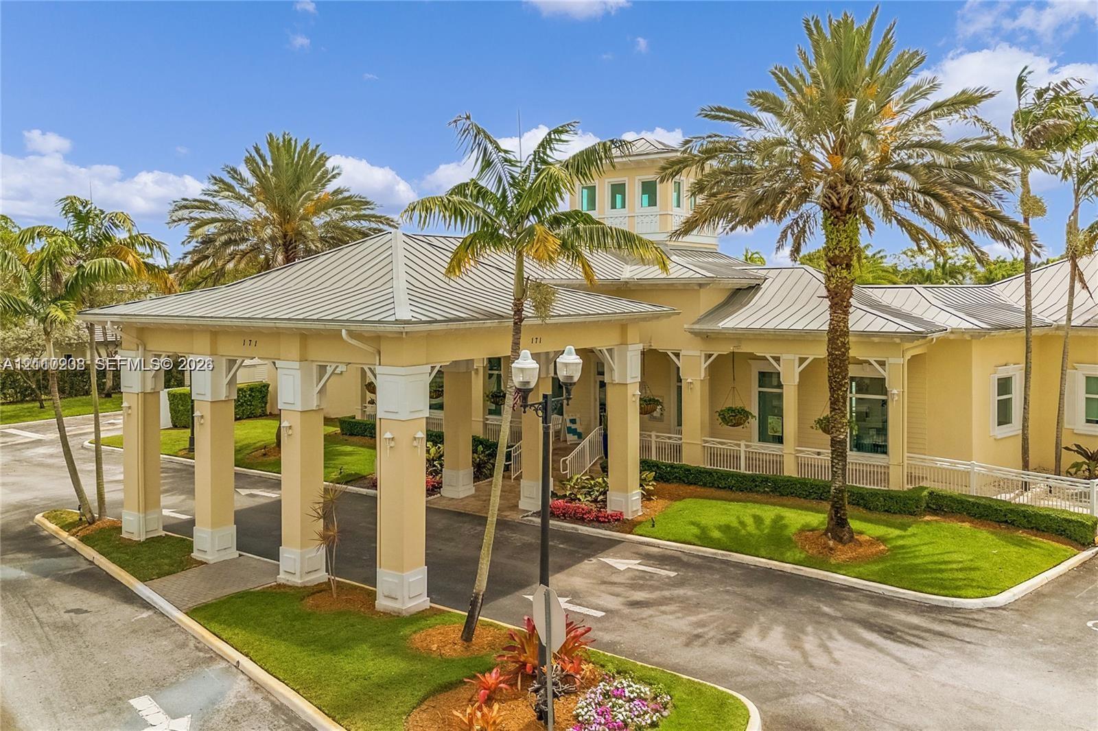 Covered porte-cochre with architectural columns, metal roof, cupola, and landscaped grounds featuring mature palm trees