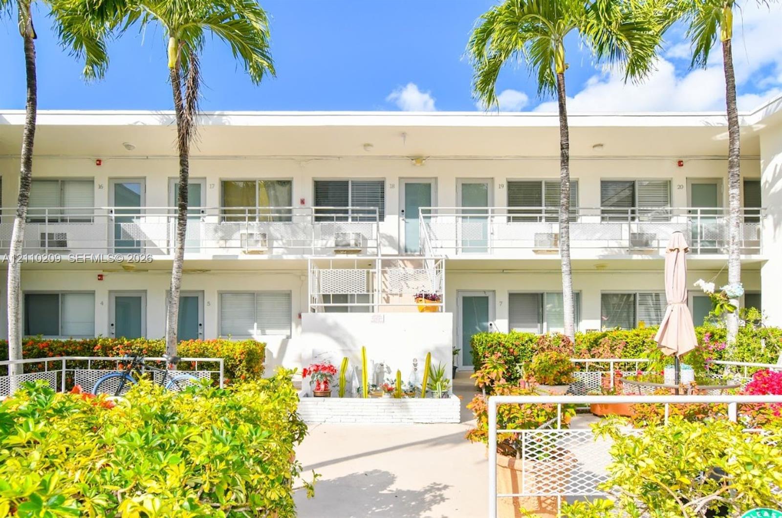 Two-story mid-century architecture featuring stucco siding, integrated second-story balcony with metal railings, and landscaped grounds with mature palm trees