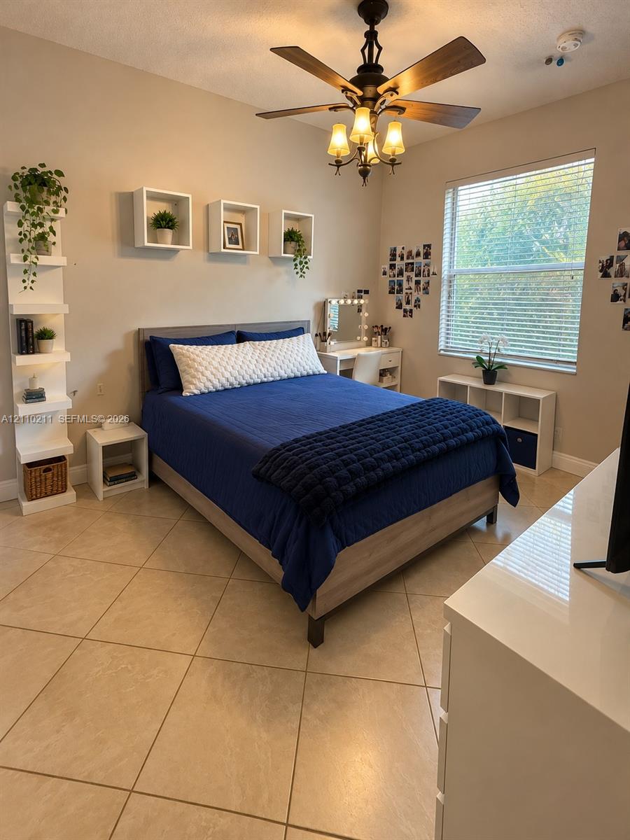 Neutral-toned interior featuring large-format tile flooring, a multi-tiered built-in corner shelf, three square floating wall-mounted shelves, and a ceiling fan with integrated multi-bulb lighting fixture