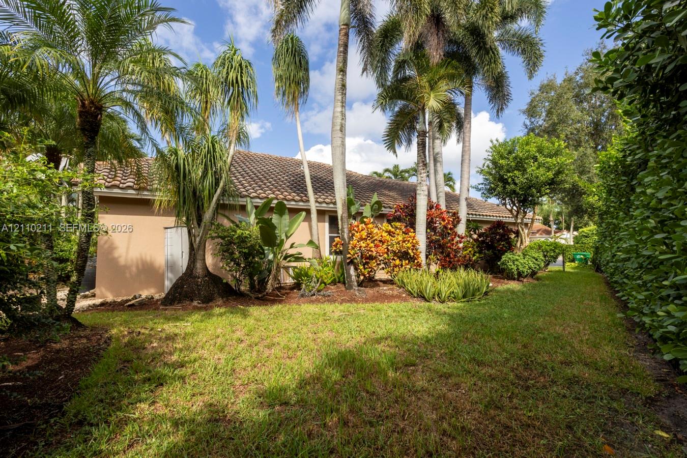 Rear exterior featuring a tile roof, mature palm trees, landscaped garden beds, and expansive lawn area