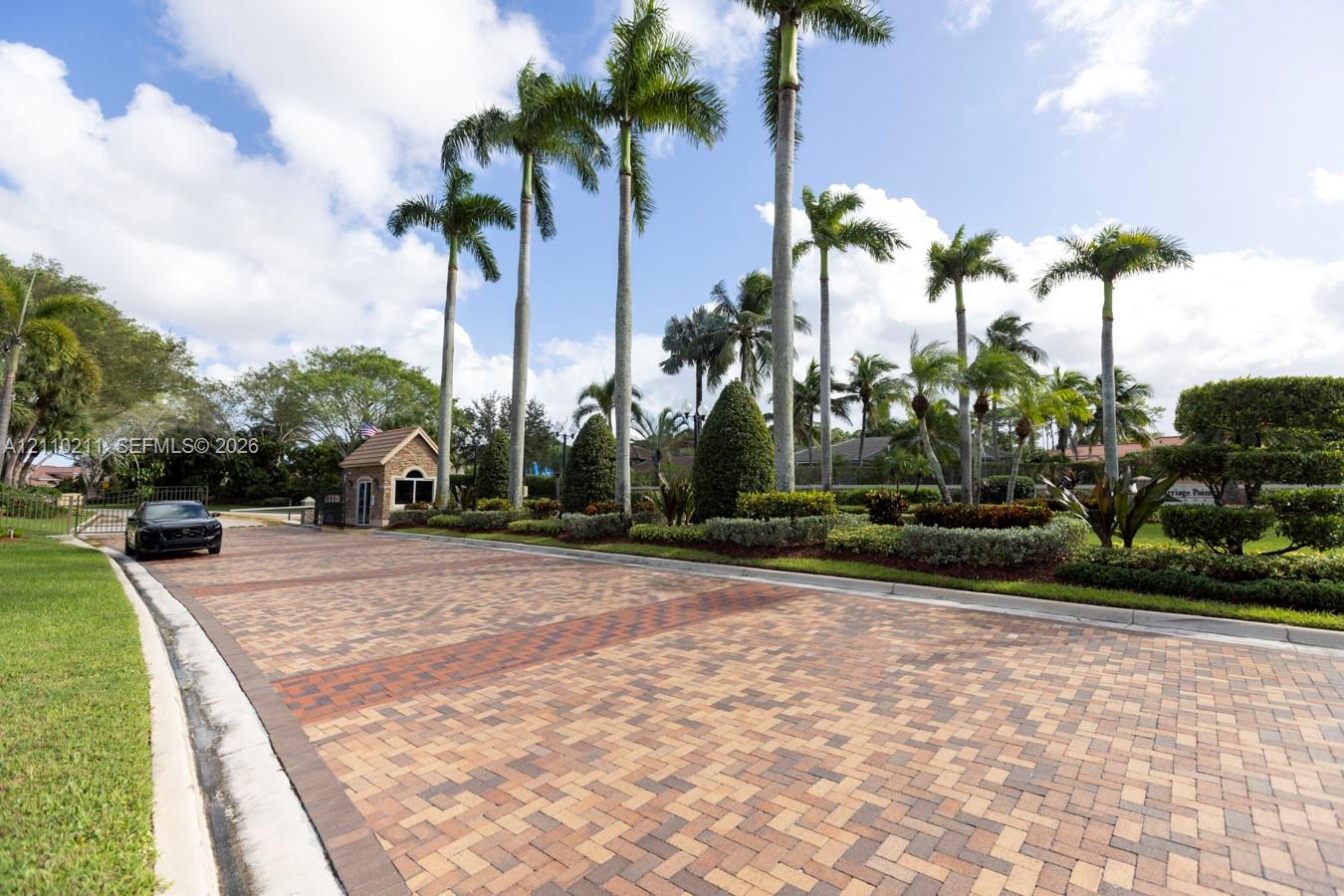 Paver-style roadway featuring a gated stone entrance, mature palm trees, manicured hedges, and professional landscaping