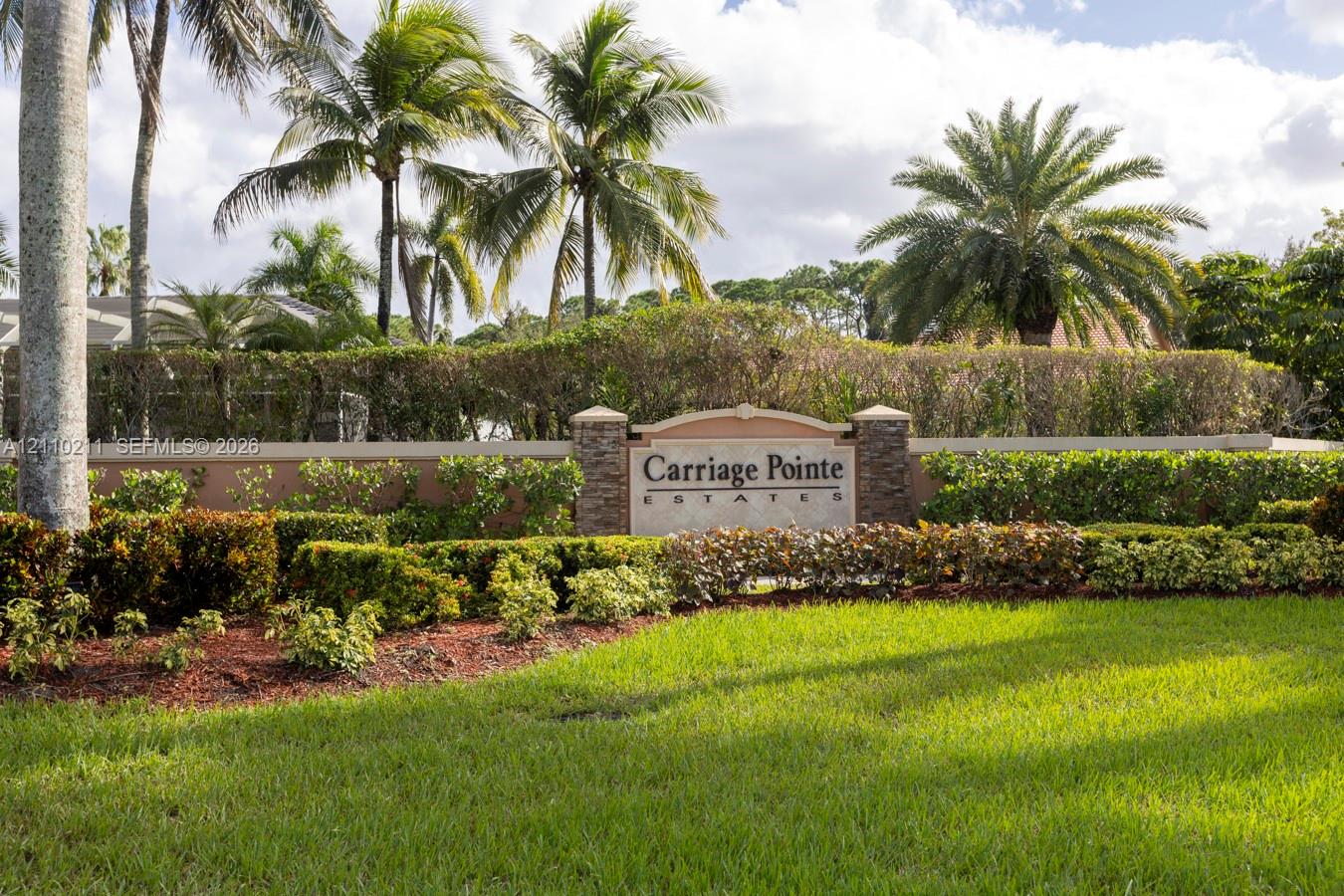 Community entrance monument featuring stacked stone pillars, stucco masonry, and extensive tropical landscaping including manicured lawn and mature palm trees