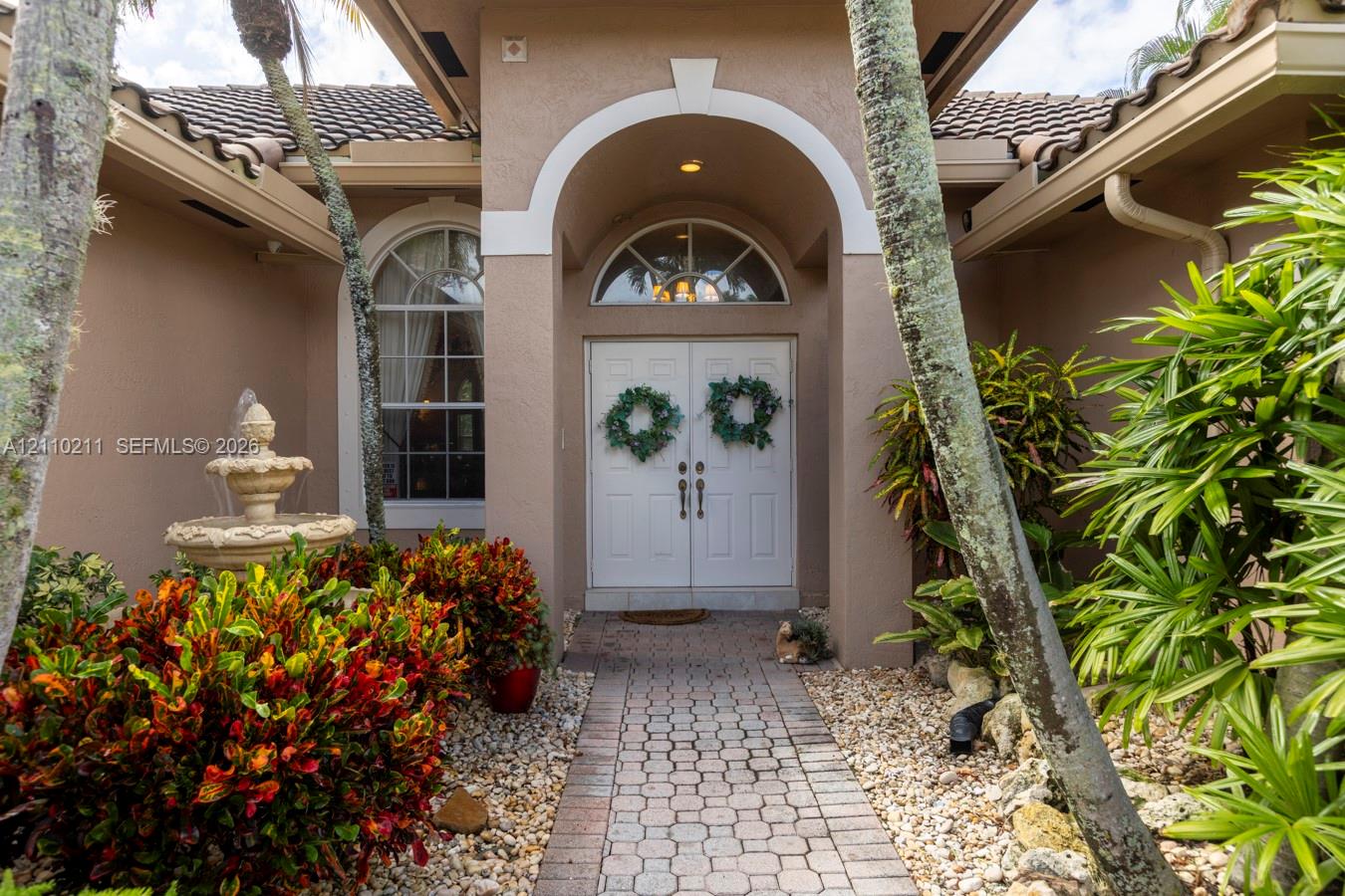 Covered entryway featuring a stone-paver walkway, arched portico, double-door entry with a semi-circular transom window, and an integrated stone fountain