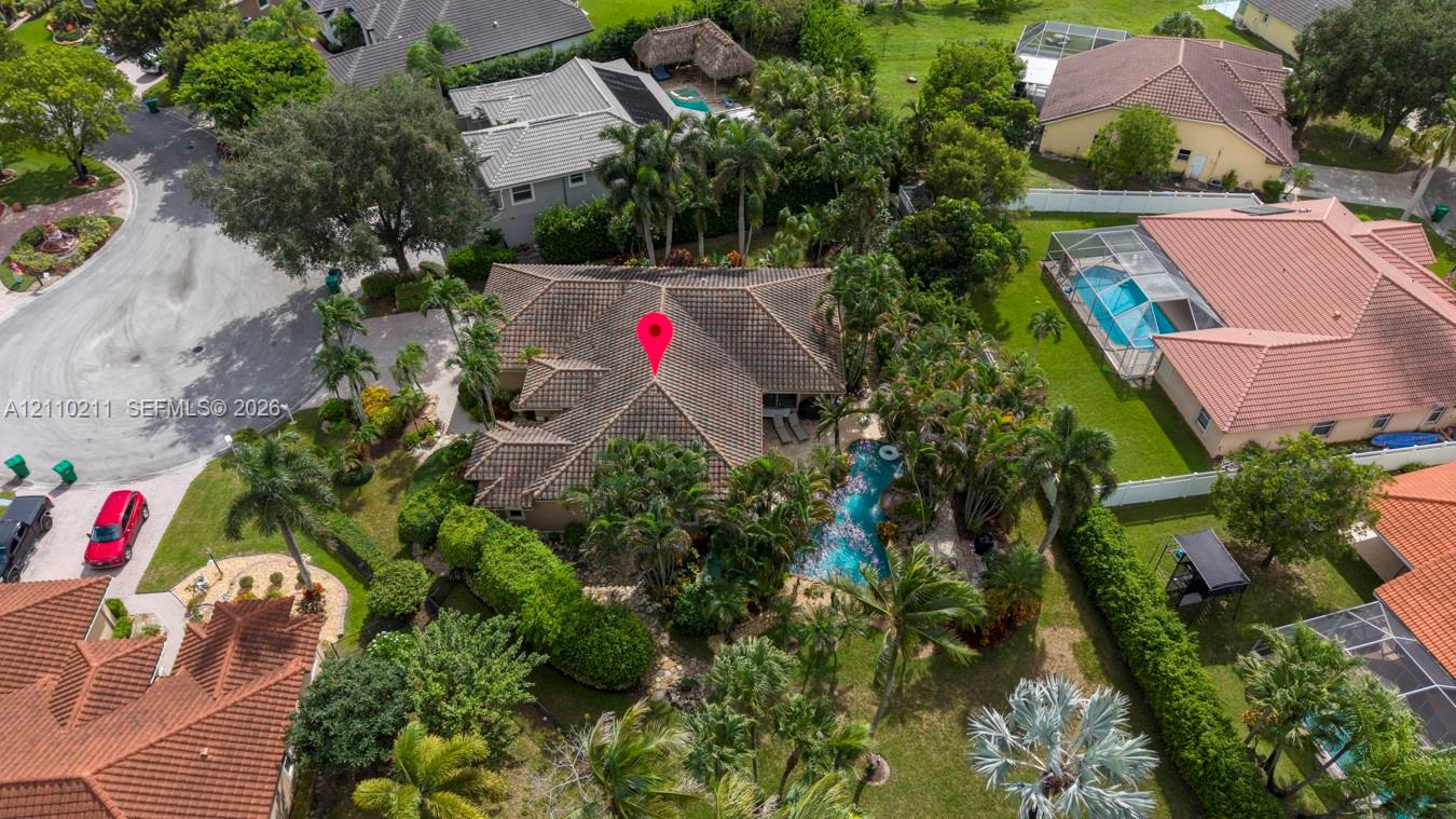 Aerial perspective of a multi-hip roof residence featuring a swimming pool, mature palm trees, dense perimeter landscaping, and a corner lot location