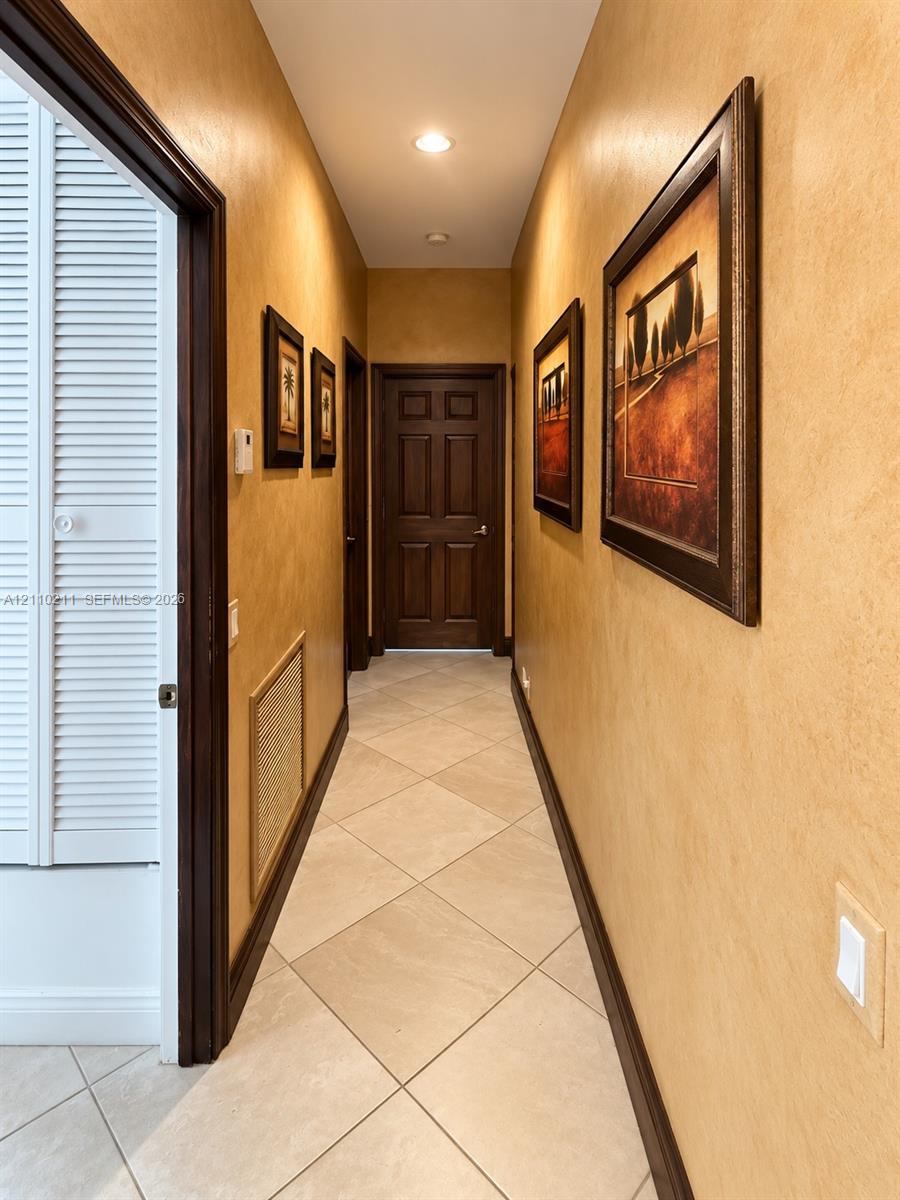 Hallway featuring neutral-toned textured wall finishes, tile flooring laid on a diagonal, recessed ceiling lighting, and solid wood-finish doors with matching trim
