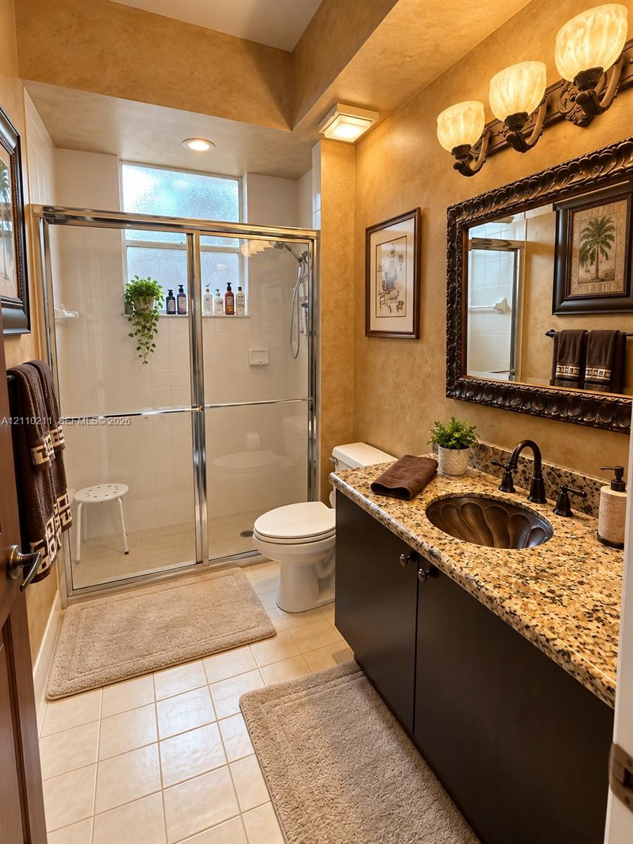 Bathroom featuring a stone-top vanity with a recessed oval basin, framed wall mirror, three-light fixture, and a glass-enclosed shower stall with a ceramic tile surround