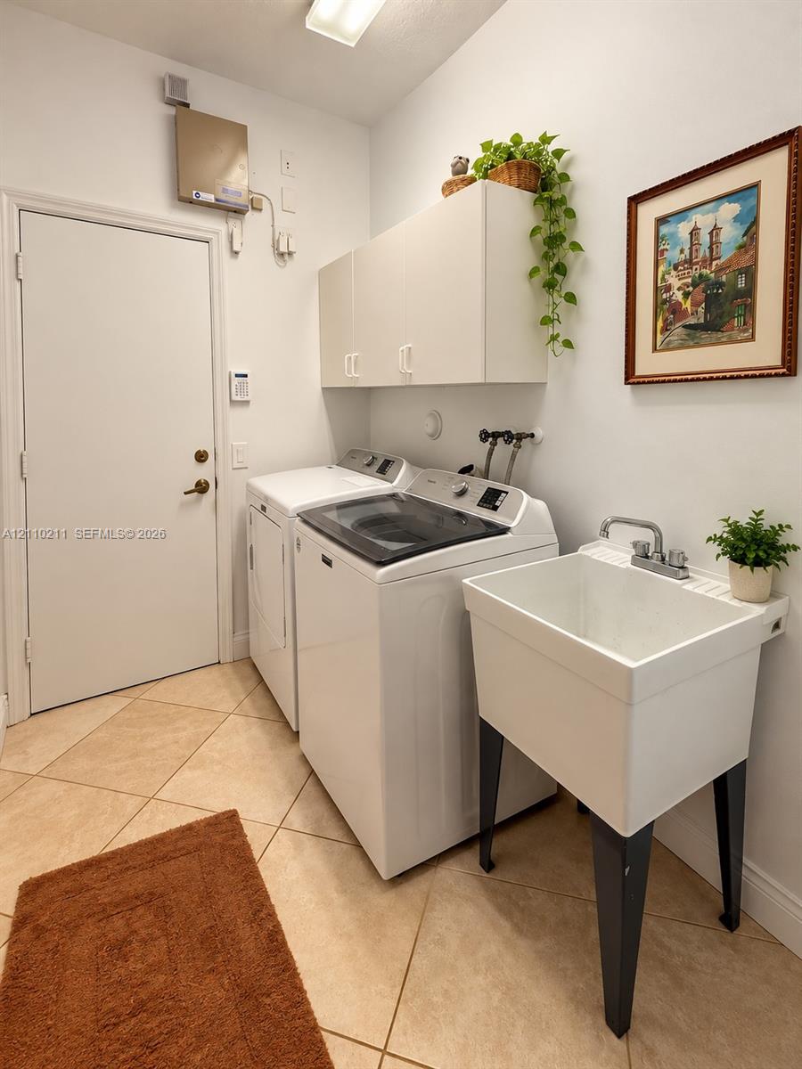 Laundry area featuring tile flooring, white built-in wall cabinetry, and a deep basin utility sink with a dual-handle faucet