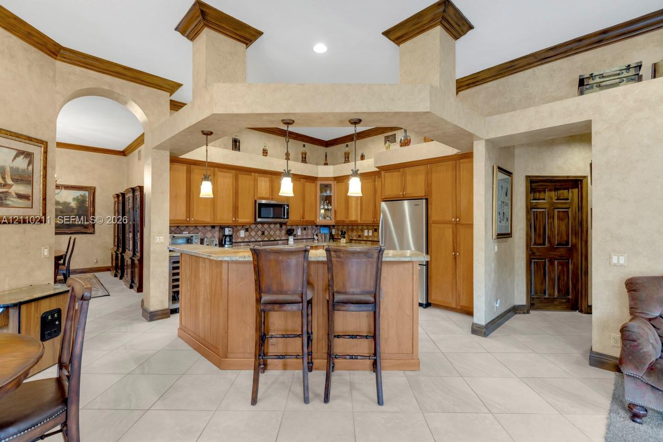 Kitchen featuring custom wood cabinetry, stone countertops, a multi-tiered peninsula island, tile flooring, and hanging pendant lighting