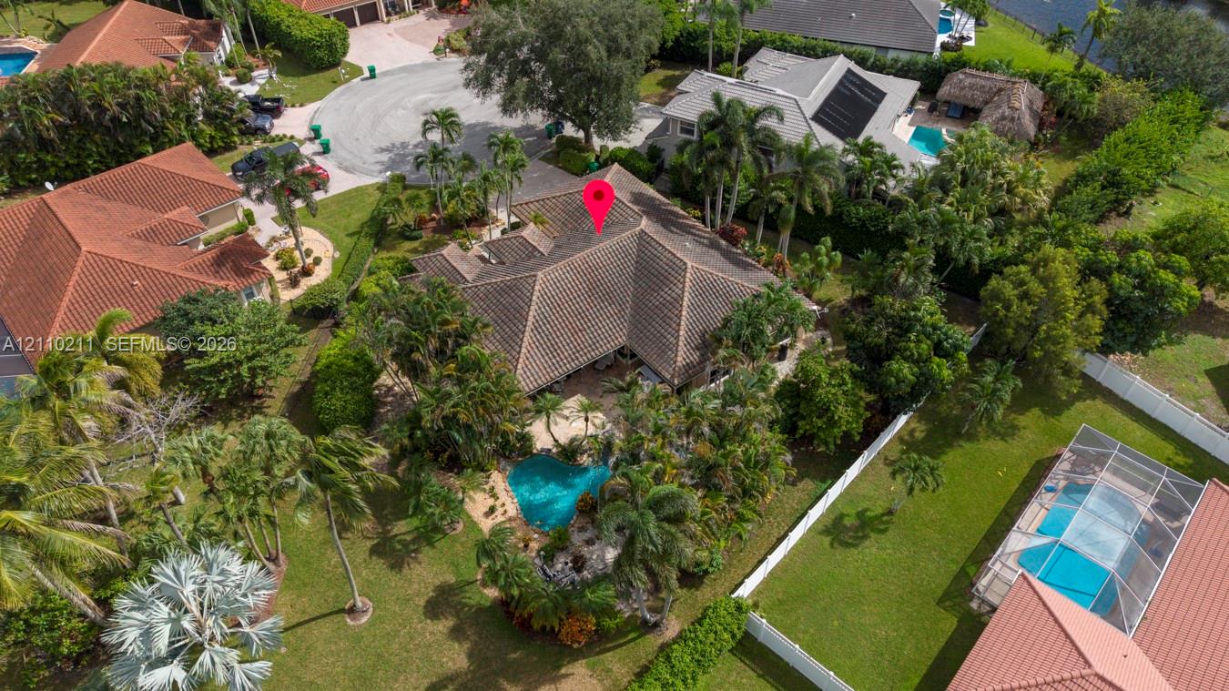 Aerial perspective featuring a tile roof, private swimming pool, mature tropical landscaping, and paved driveway