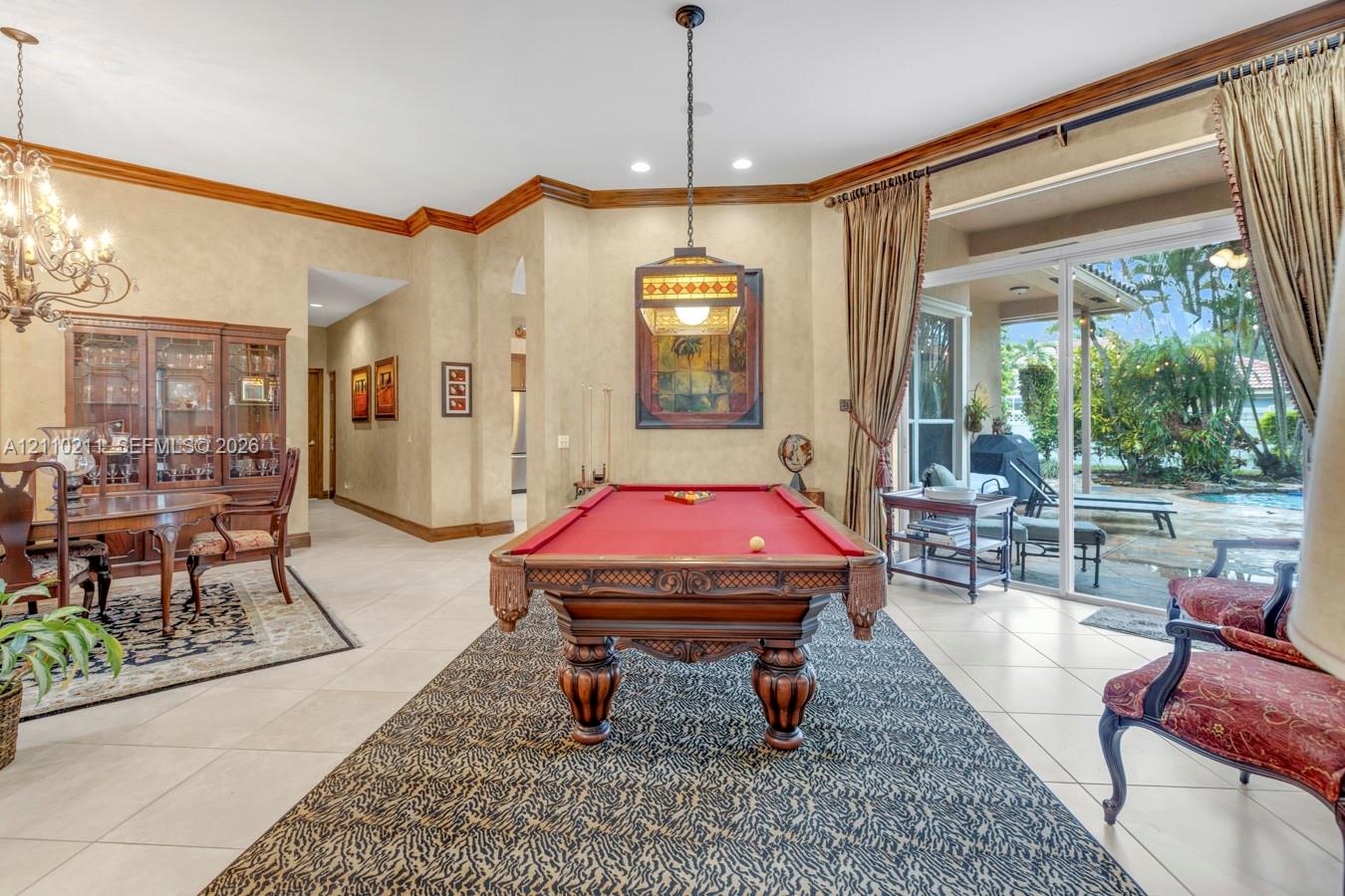 Spacious room featuring neutral tile flooring, crown molding, a decorative multi-light chandelier, a stained-glass style pendant fixture, and large sliding glass doors