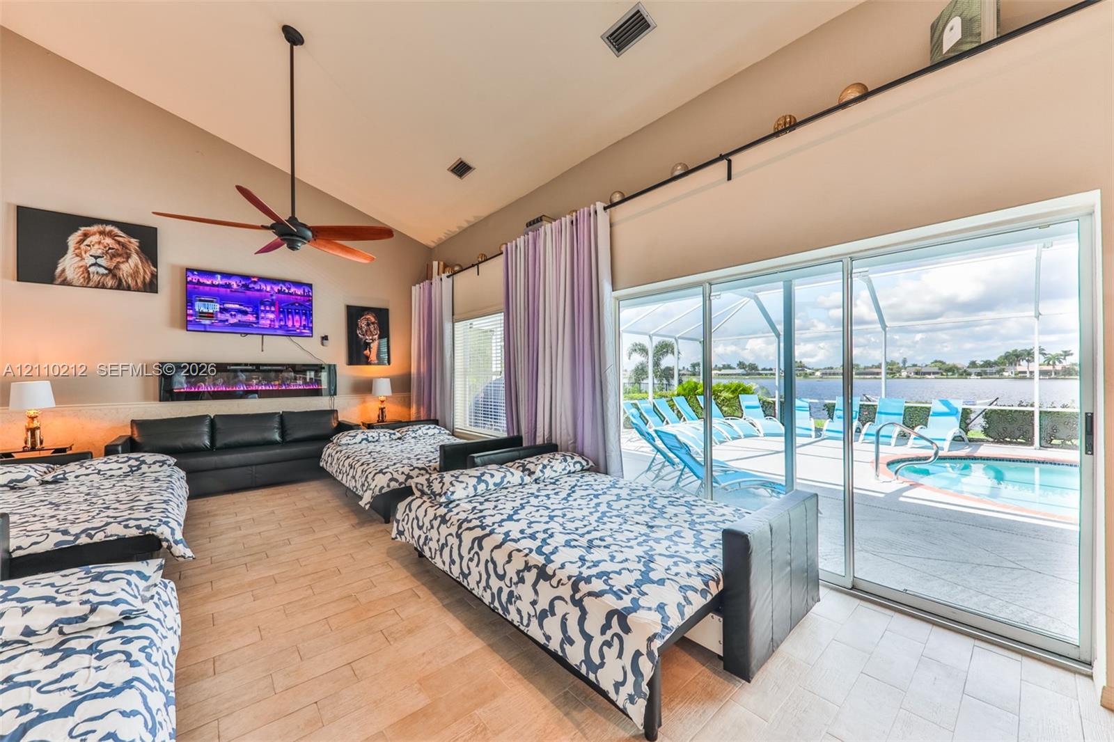 Vaulted ceilings, built-in electric wall fireplace, wood-finish tile flooring, ceiling fan, and large sliding glass doors providing outdoor access