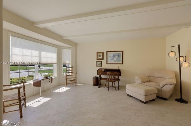 Light-filled room featuring neutral tile flooring, exposed ceiling beams, and a prominent bay window with cellular shades