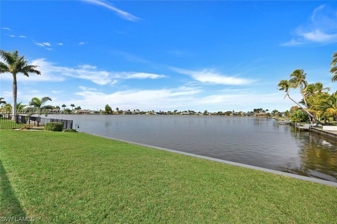 Waterfront lot featuring a manicured lawn, concrete seawall, and mature palm trees