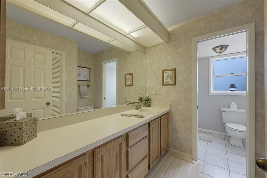 Full-width vanity featuring wood-finish cabinetry, solid surface countertop with integrated basin, expansive wall-to-wall mirror, and overhead soffit lighting