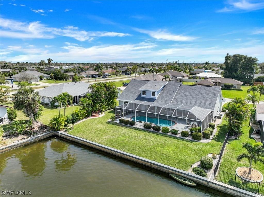 Waterfront property featuring a screened-in lanai with a swimming pool, concrete seawall, and landscaped lawn Waterfront property featuring a screened-in lanai with a swimming pool, concrete seawall, and landscaped lawn