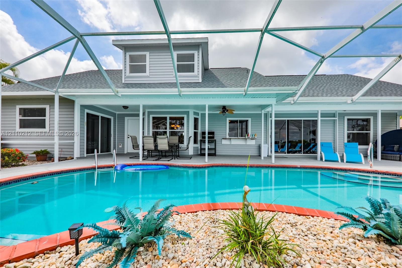 In-ground swimming pool with brick-style coping, enclosed by a screened lanai with a covered patio area featuring a built-in outdoor service counter and ceiling fan