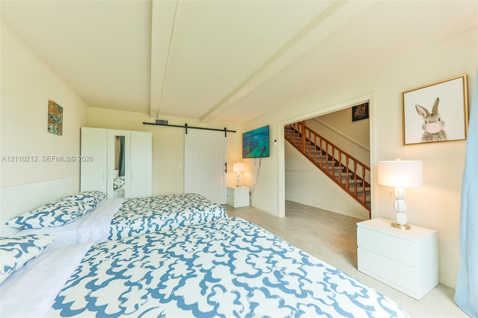 Room featuring neutral wall tones, exposed structural ceiling beams, a sliding barn-style door, and light-toned flooring