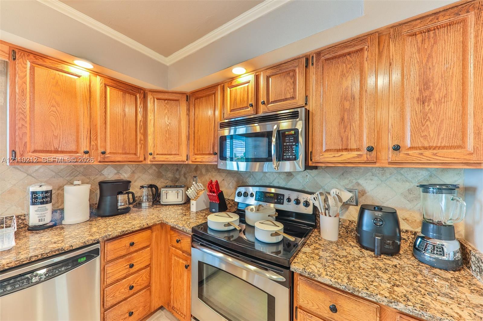 Kitchen featuring medium-tone wood cabinetry, stone-surface countertops, stone tile backsplash, and stainless steel appliances including a built-in microwave and range