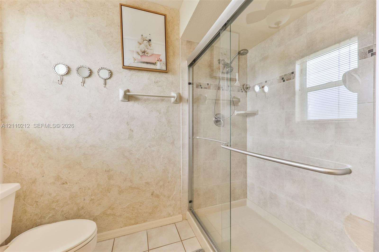 Walk-in shower enclosure with a sliding glass door, neutral-toned tiled walls, a built-in corner shelf, and a polished metal shower fixture