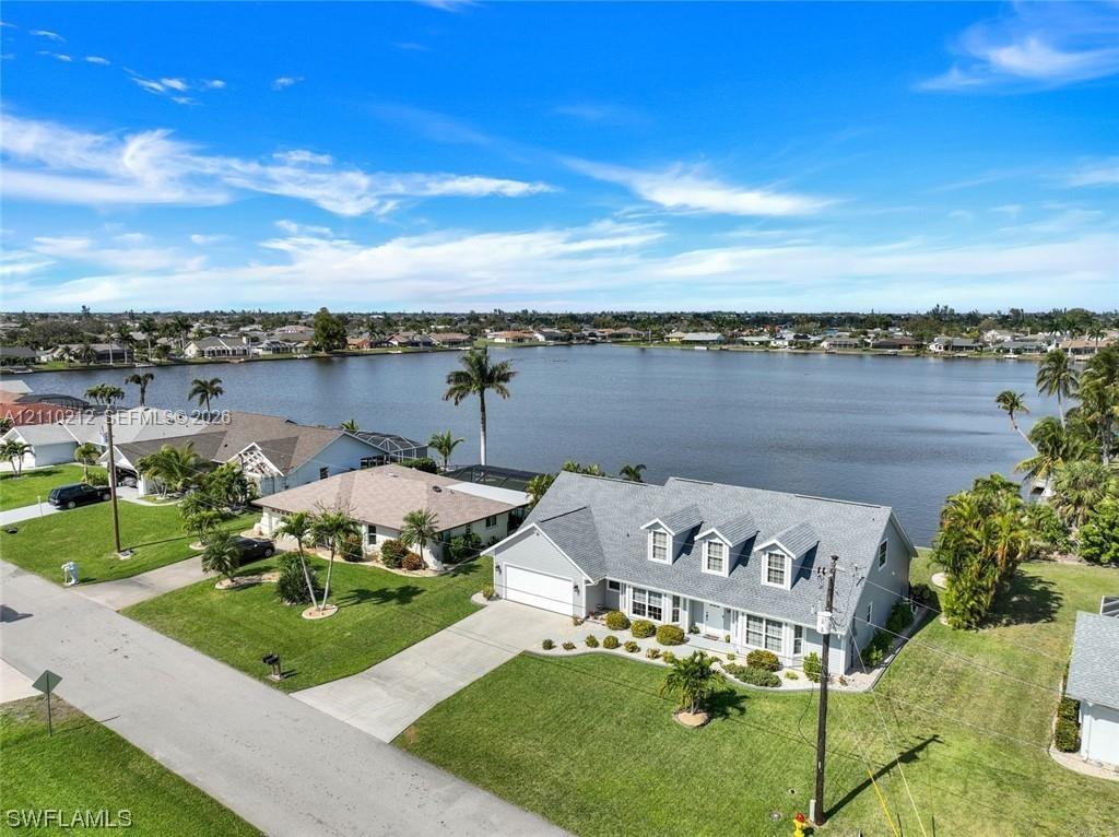 Waterfront property featuring a multi-gable roofline, attached two-car garage, concrete driveway, and expansive lawn area