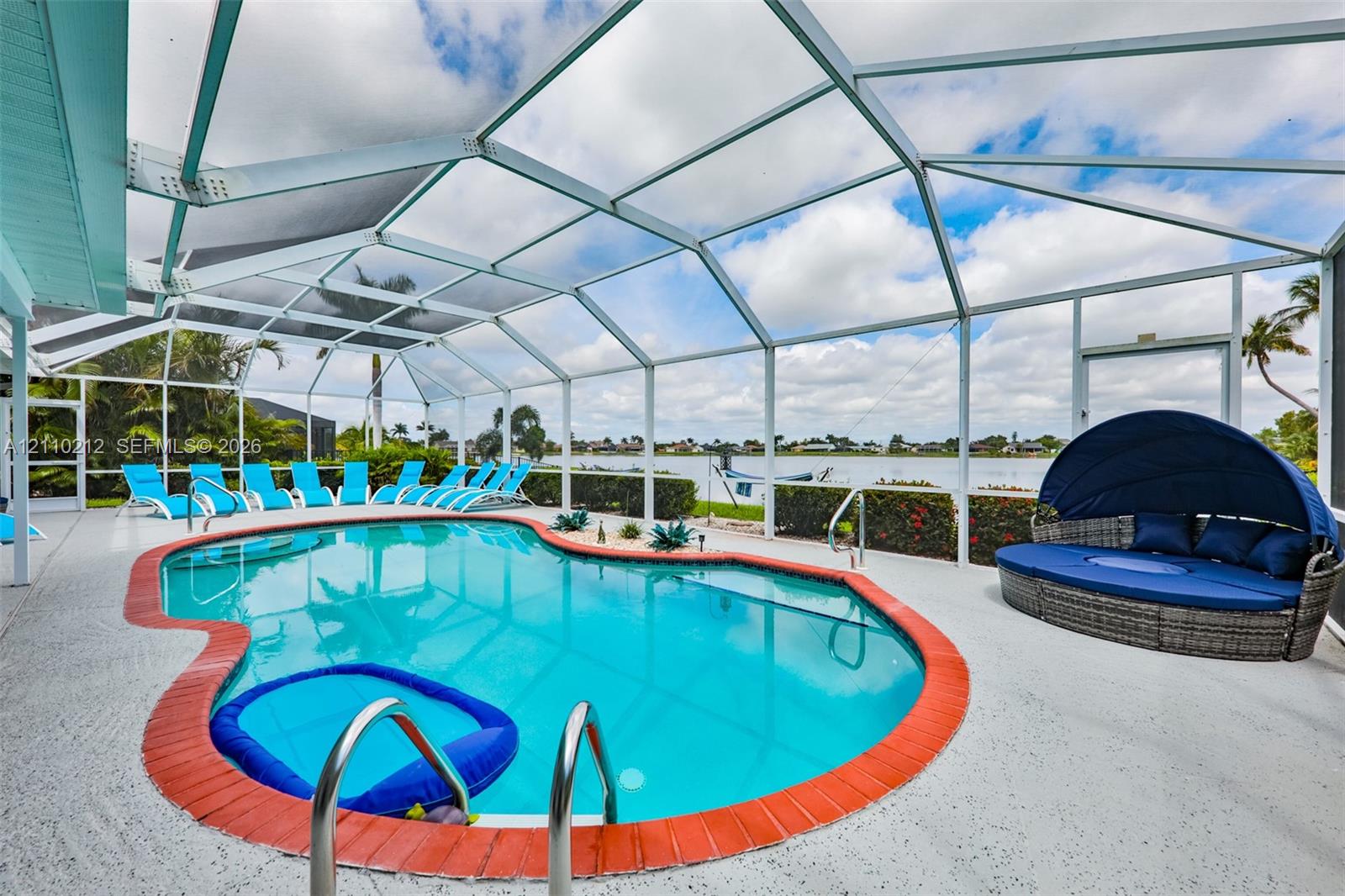 Screen-enclosed swimming pool featuring a brick-paver border, concrete decking, metal pool ladder, and waterfront positioning