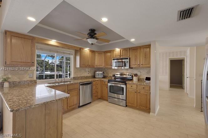 Kitchen featuring light wood cabinetry, stone-finish countertops, stainless steel appliances, a recessed tray ceiling, and tile flooring