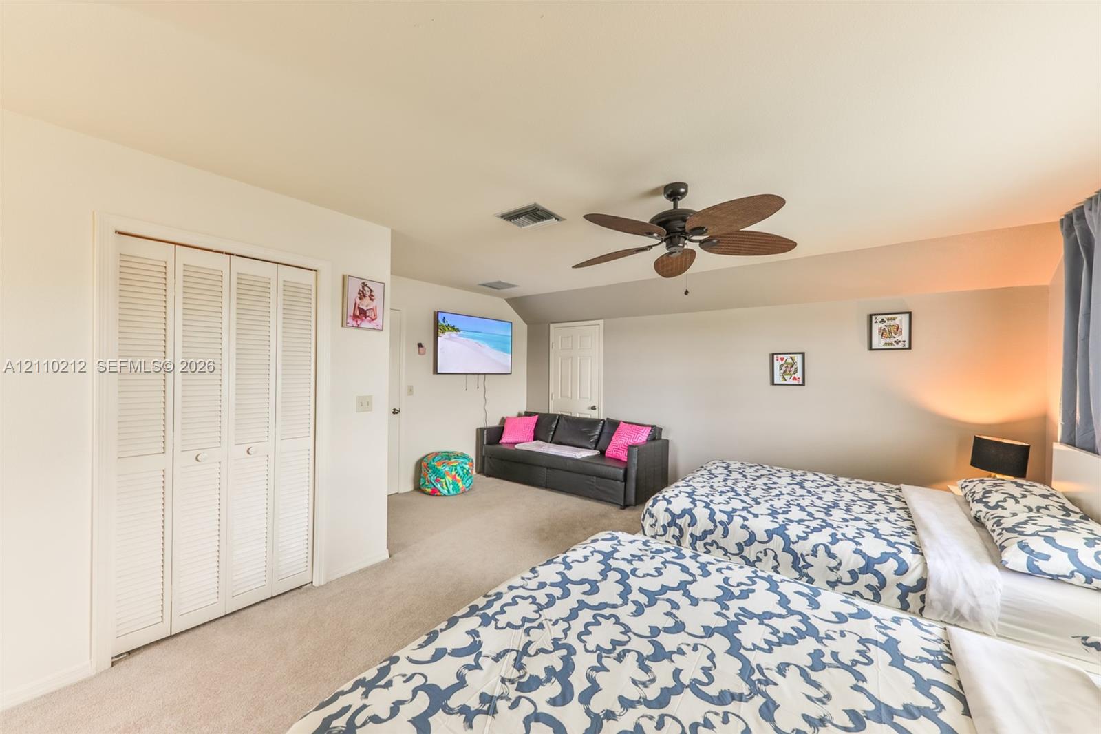 Spacious room featuring neutral carpeting, multi-panel louvered closet doors, and a ceiling fan with integrated lighting