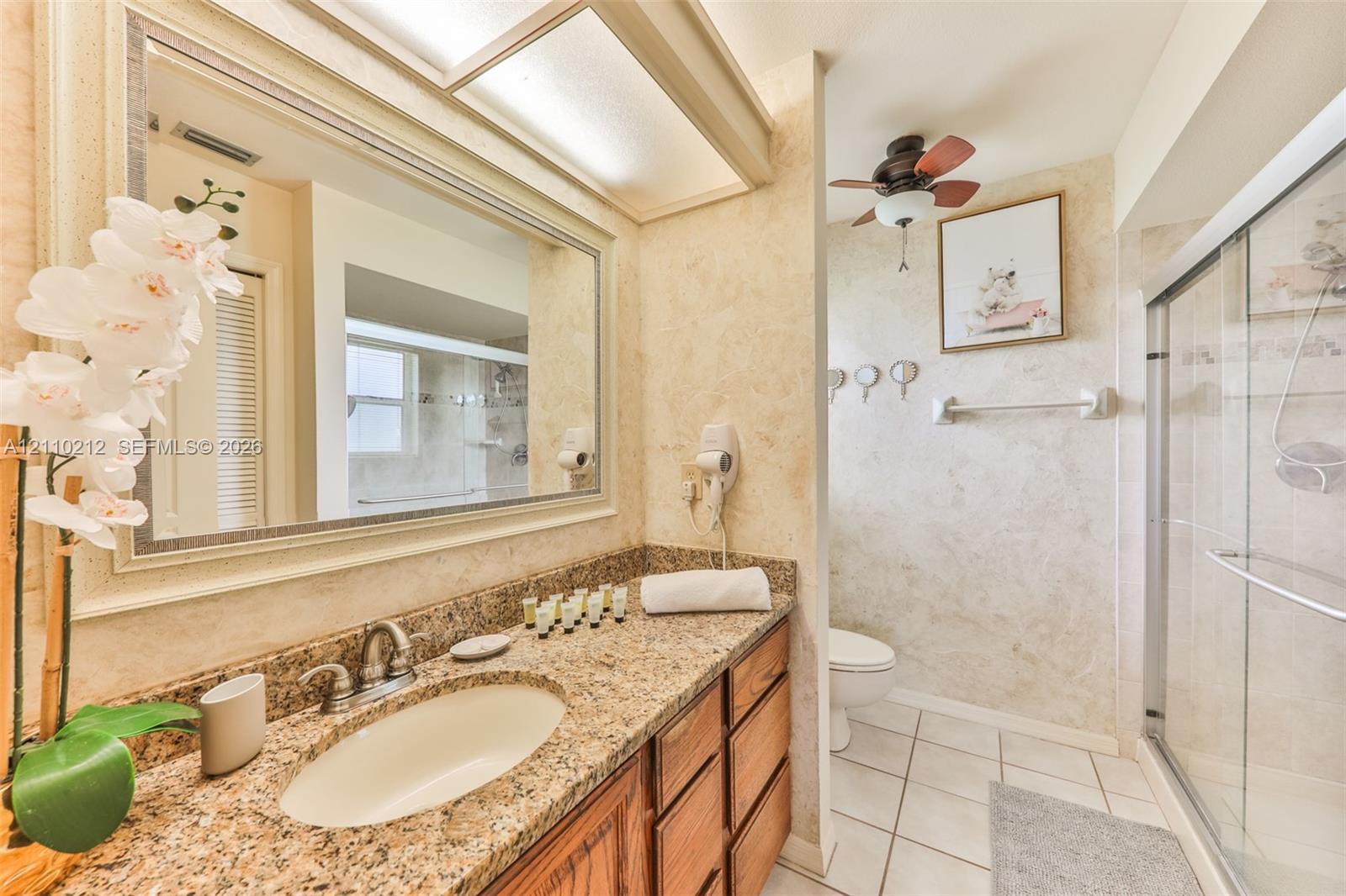 Stone countertop with integrated oval sink, wood-finish cabinetry, framed vanity mirror, overhead lighting fixture, and a glass-enclosed shower