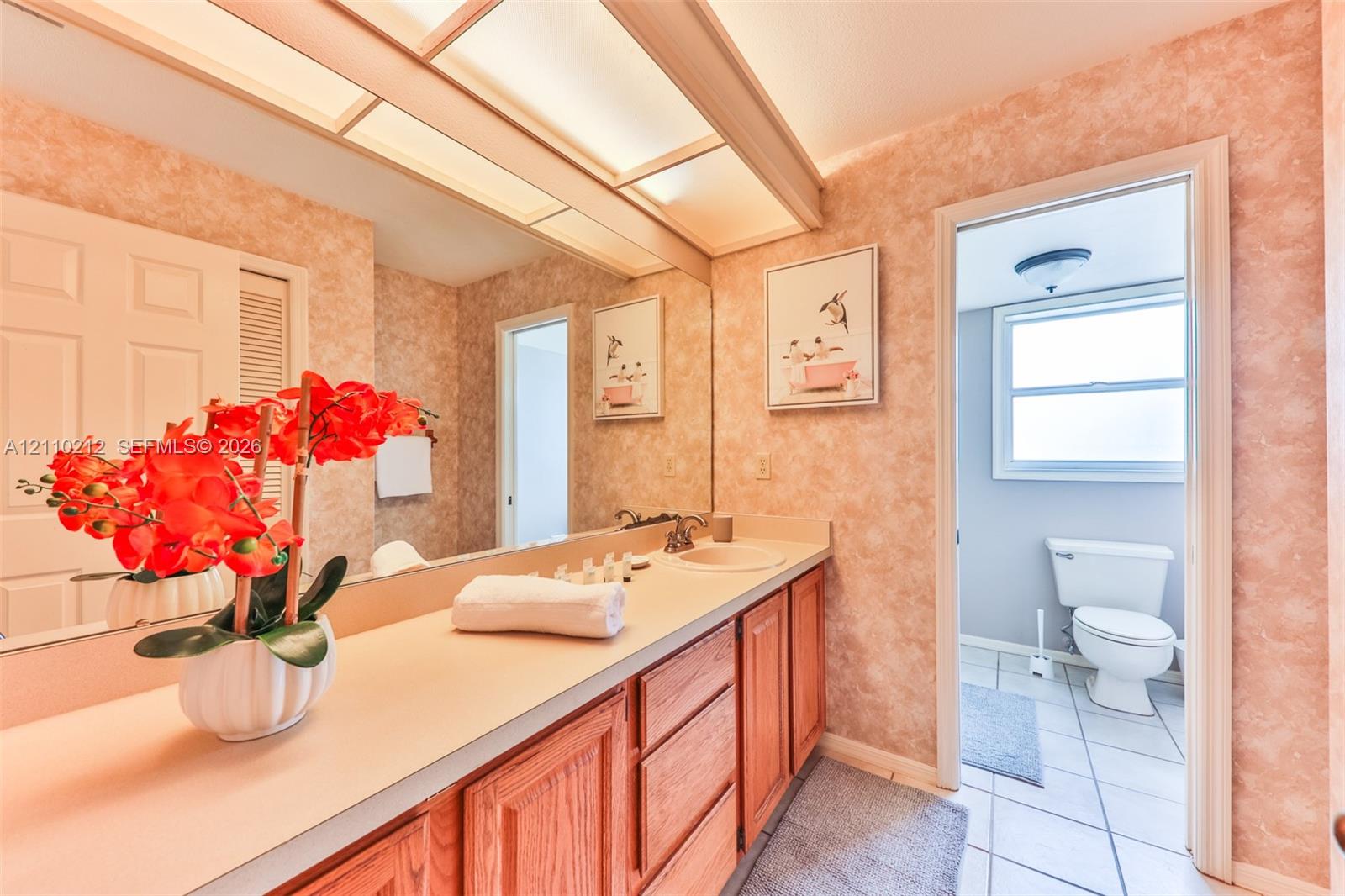 Bathroom featuring wood cabinetry, solid-surface countertop with an integrated sink, full-width wall mirror, and overhead soffit lighting