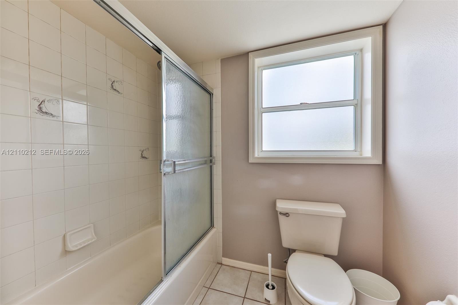 Full bathroom featuring a shower-tub combination with sliding glass doors, square-tile wall surround, framed window, and ceramic floor tiling