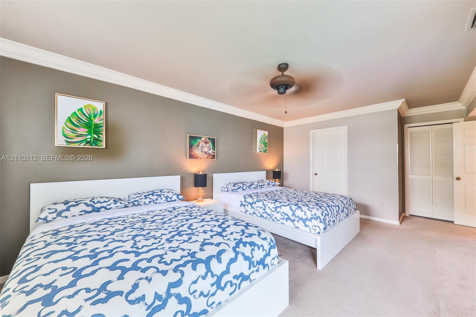 Room featuring an accent wall, crown molding, wall-to-wall carpeting, a ceiling fan, and double-door closet storage